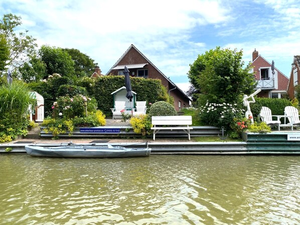 A canal with a rowboat docked, a bench, and a building with a sign. - SIELBLICK: Schicke Ferienwohnung mit Balkon und herrlichem Sielblick (Greetsiel)