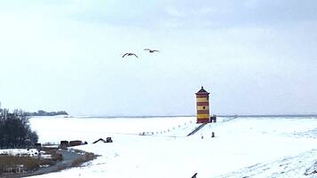A snow-covered landscape with a tall, narrow lighthouse and a few birds flying in the sky.