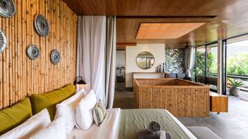 Una habitación de hotel moderna con pared de bambú, un mostrador de recepción de madera y un ventanal con vistas a la vegetación.