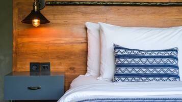 Una cama bien hecha con almohadas blancas y estampadas, una mesita de noche con lámpara y un cabecero de madera.