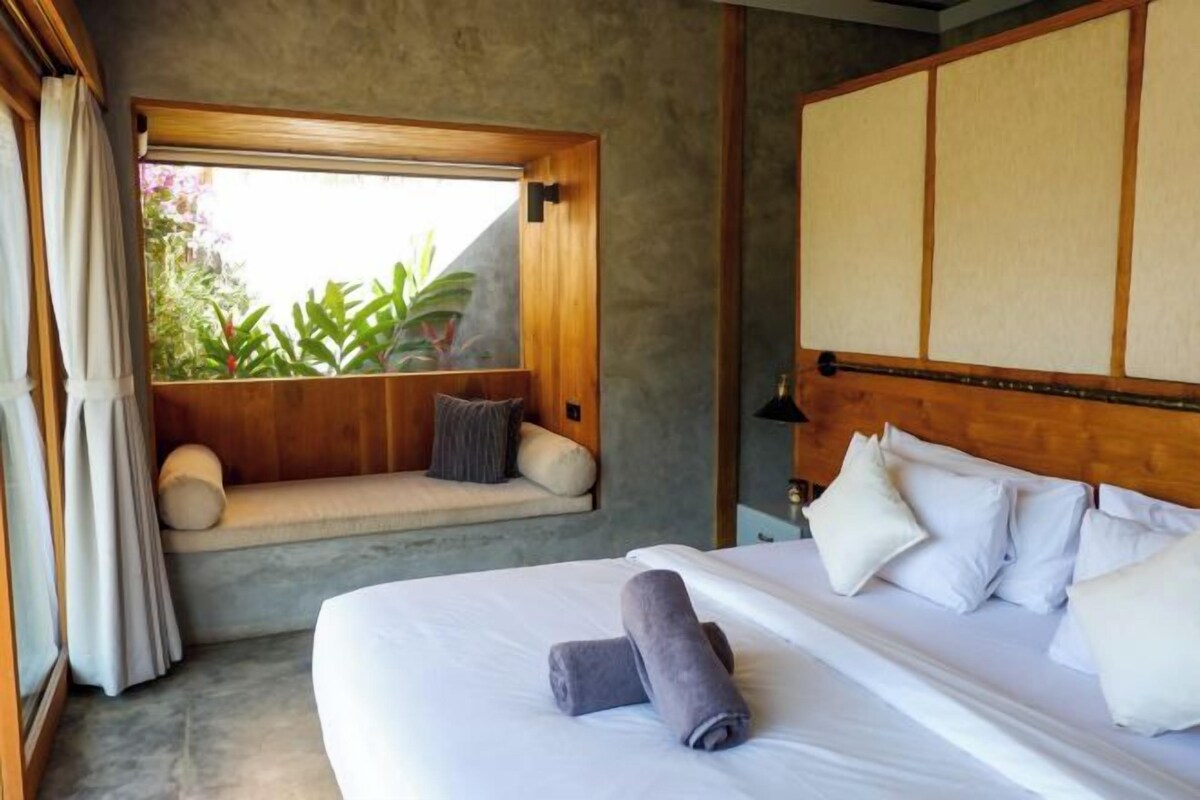 Une chambre d’hôtel avec un grand lit, un coin fenêtre agrémenté de coussins et une tête de lit de style japonais traditionnel.