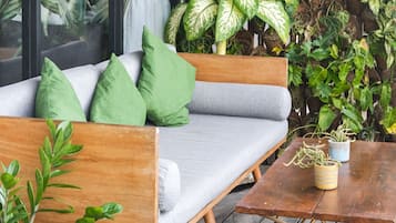 A wooden deck with a grey sofa and green cushions, surrounded by a variety of potted plants and a vertical garden.