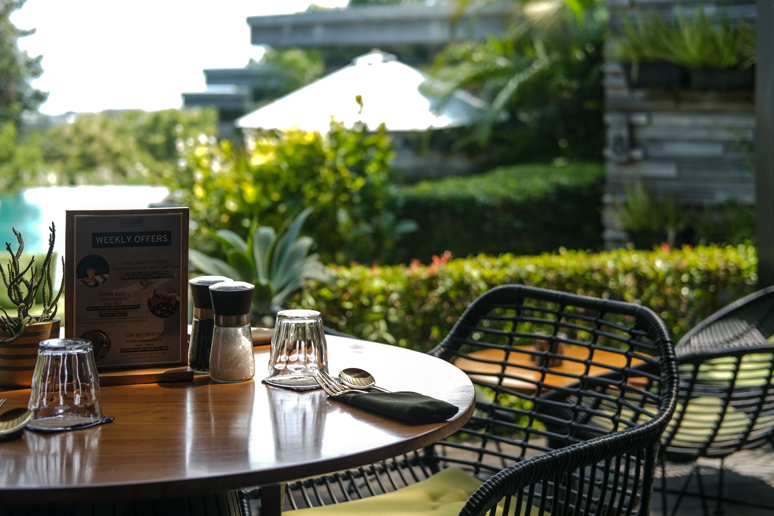 A round wooden table with a menu board, salt and pepper shakers, a glass, and cutlery.
