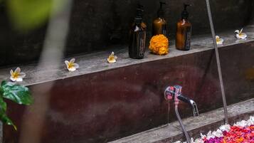 Un bagno con una vasca da bagno circondata da petali colorati, un soffione e articoli da toilette su uno scaffale.