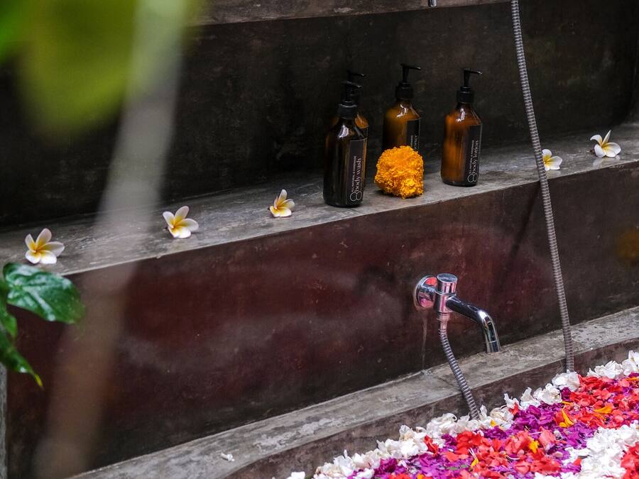 Un bagno con una vasca da bagno circondata da petali colorati, un soffione e articoli da toilette su uno scaffale.