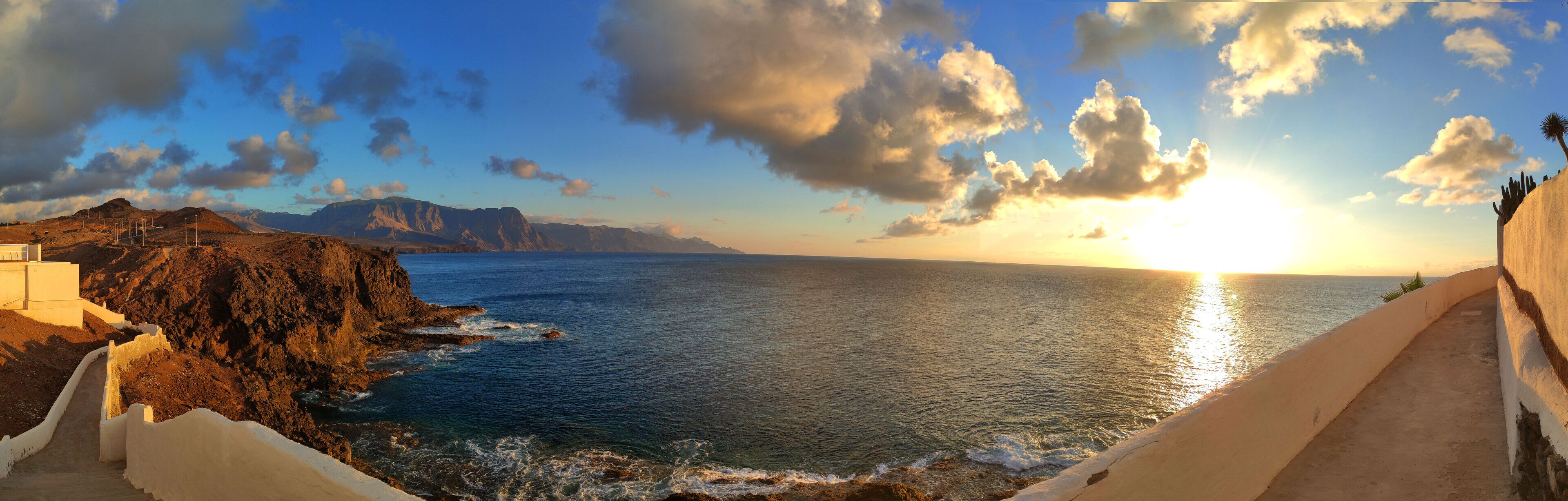 A coastal landscape with a clear sky, a sunset, and rocky terrain.