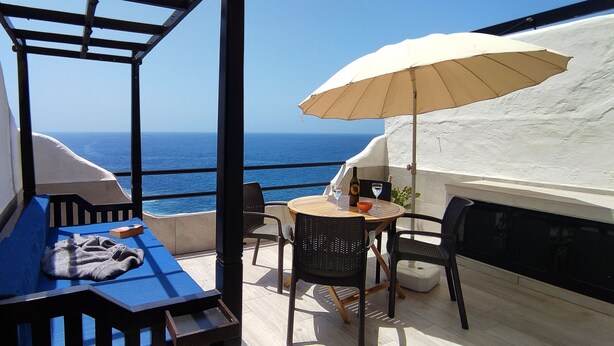 A balcony with a view of the sea, a table with chairs, and a beige umbrella. - Relax in front of the Ocean with a beautiful view! (Sardina del Norte)