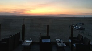 A terrace with outdoor seating and a view of the sunset over a flat landscape.