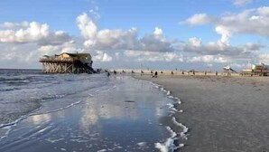 A beach with a pier extending into the water, a few people walking, and a clear sky.