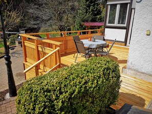 A wooden deck with a table and chairs, surrounded by a wooden fence and a hedge. - Holiday house "Trudi", a place to relax, also with a dog (Fambach)