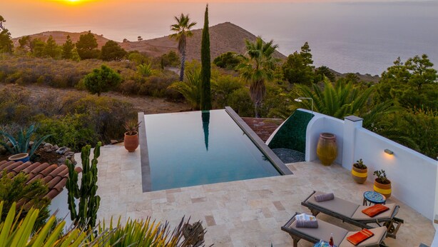 Ein Pool auf dem Dach mit Blick auf das Meer und die Hügel, umgeben von Pflanzen und Gartenmöbeln.