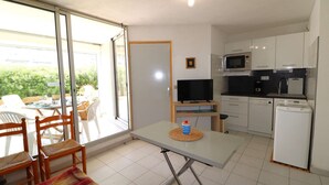 A compact kitchen with white cabinets, a microwave, a coffee maker, and a refrigerator. There is a dining area with a table and chairs, and a sliding glass door leading to an outdoor patio. - 2 rooms cabin on the ground floor terrace (LE GRAU DU ROI)