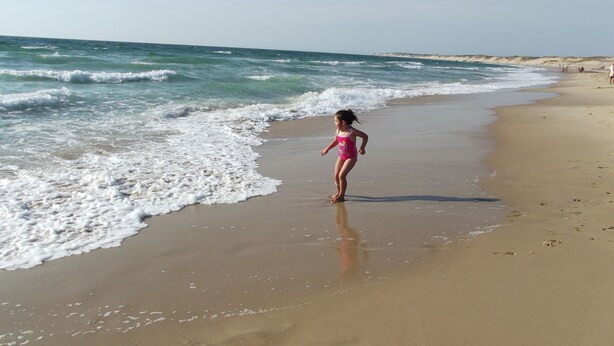 Una playa con olas, una persona en traje de baño y huellas en la arena.