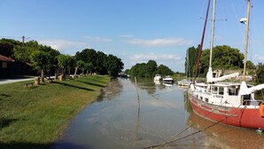 Un canal estrecho con barcos amarrados a la derecha, una orilla cubierta de hierba a la izquierda y árboles al fondo.