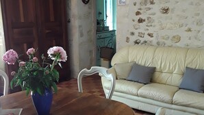 Una sala de estar acogedora con una mesa redonda de madera, un jarrón azul con flores, un sofá color crema y un suelo a cuadros.
