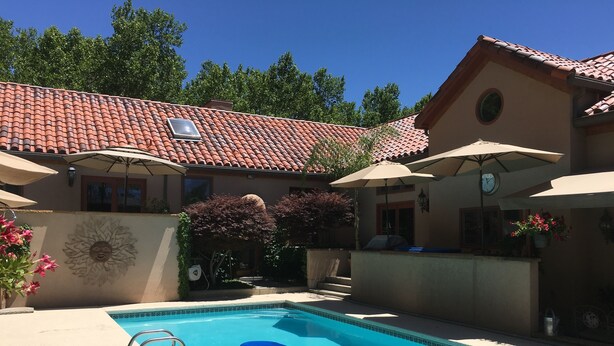 A swimming pool with blue floating mats, surrounded by umbrellas and a building with a tiled roof.