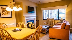 A living room with a fireplace, a sofa, a dining table with chairs, and a TV mounted on the wall.