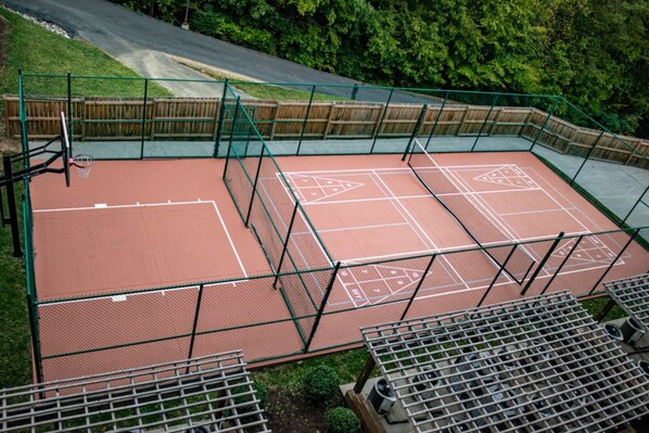 An outdoor tennis court with a green fence, surrounded by a wooden fence and trees. - Pigeon Forge | Smoky Mountain Villa | Spa + Pool (Pigeon Forge)