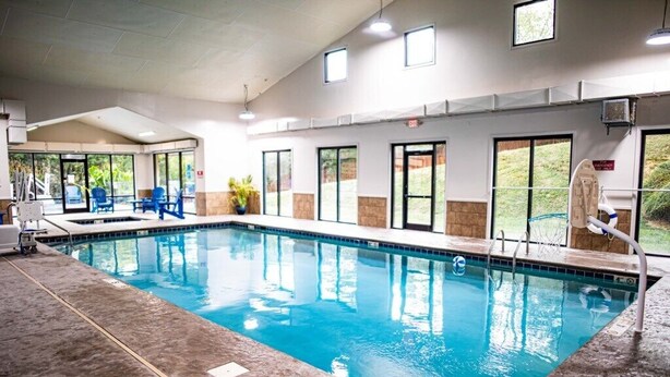 An indoor swimming pool with clear water, surrounded by blue chairs and a concrete floor.