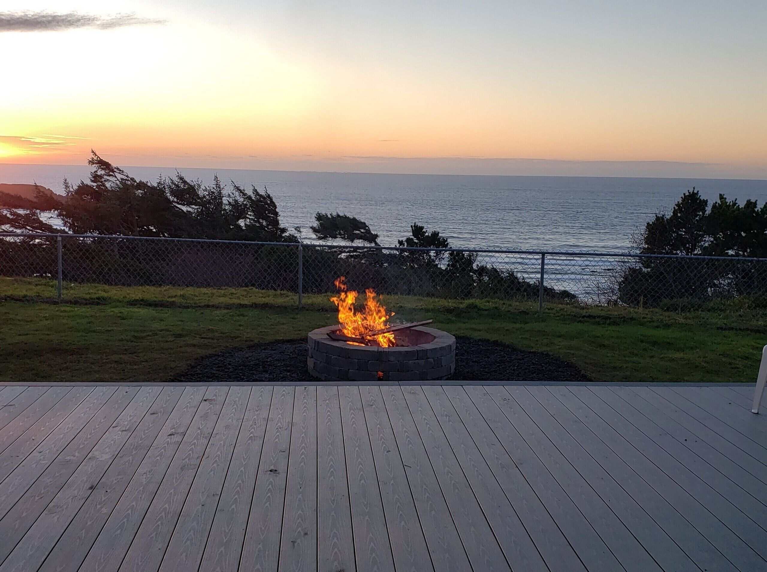 A deck with a fire pit and a view of the ocean at sunset.