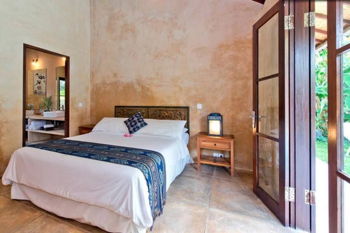 A bedroom with a bed, nightstand, and a large window.