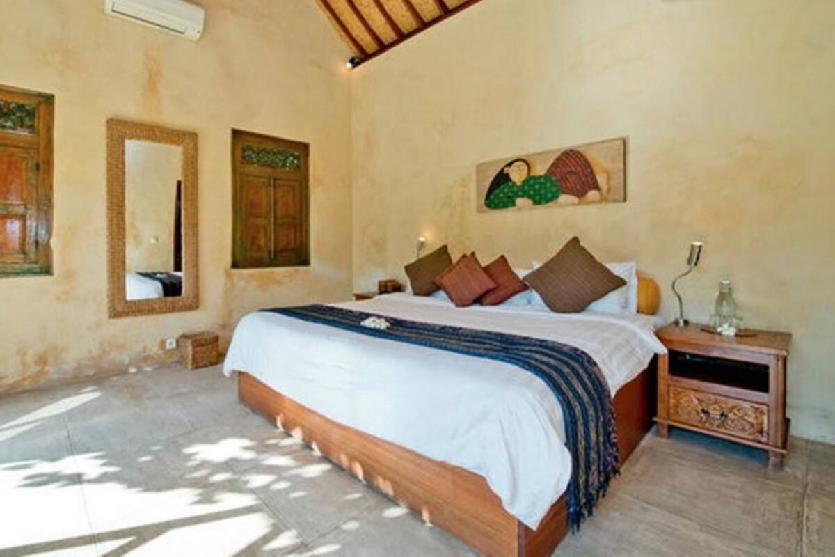 A bedroom with a large bed, wooden headboard, two nightstands, a mirror, and a wall-mounted artwork.