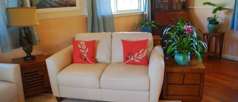 Un salón con un sofá beige, cojines rojos, un aparador de madera y una planta en maceta.