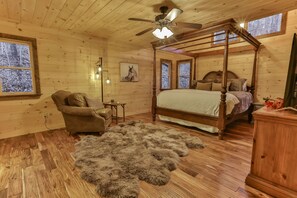 Un dormitorio de cabaña de madera con cama con dosel, ventilador de techo y alfombra de piel.