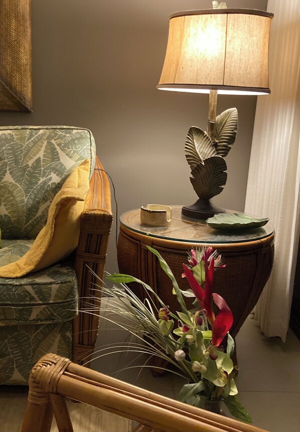 Une pièce comprenant un fauteuil en osier, une petite table ronde avec une lampe et un arrangement floral.