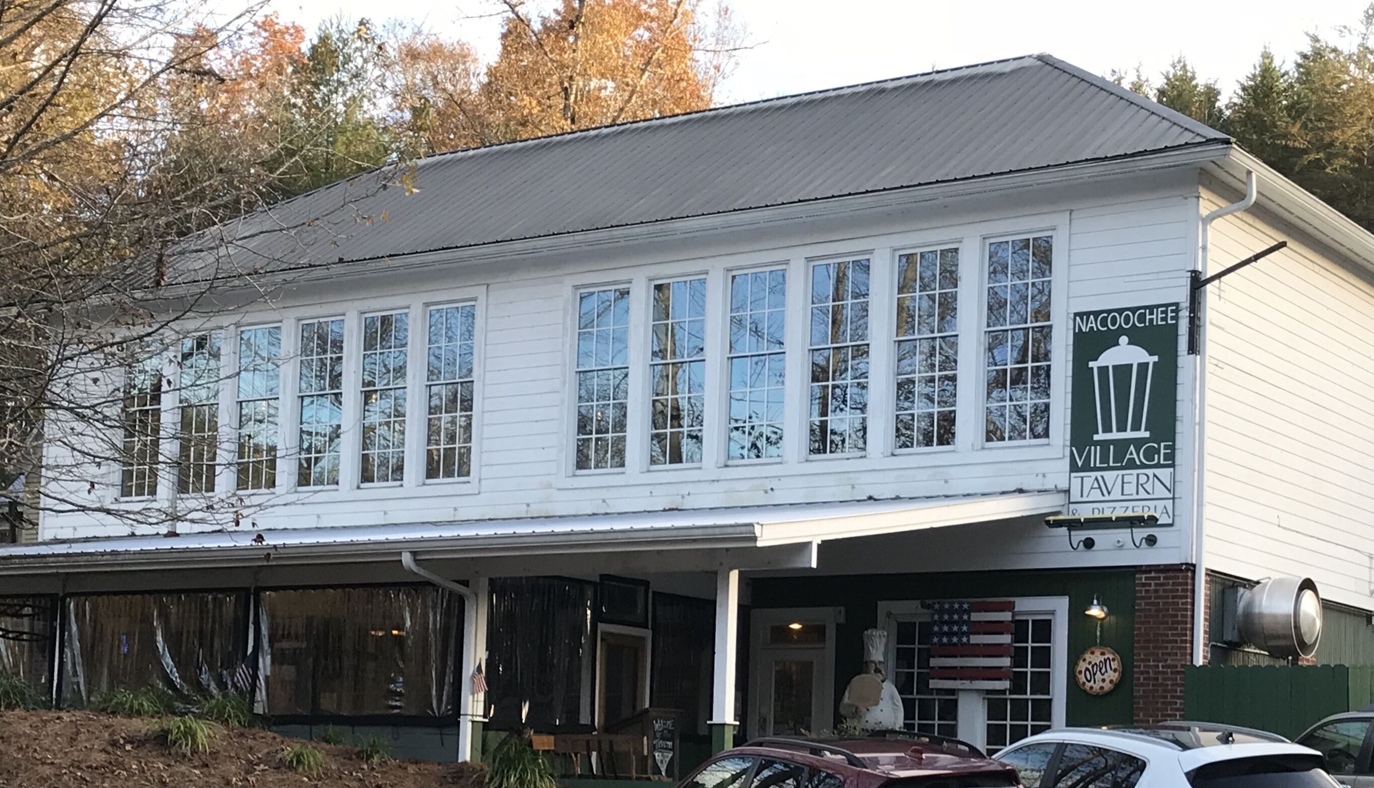 Un edificio blanco con ventanas grandes y un cartel que dice Nacoochee Village Tavern.