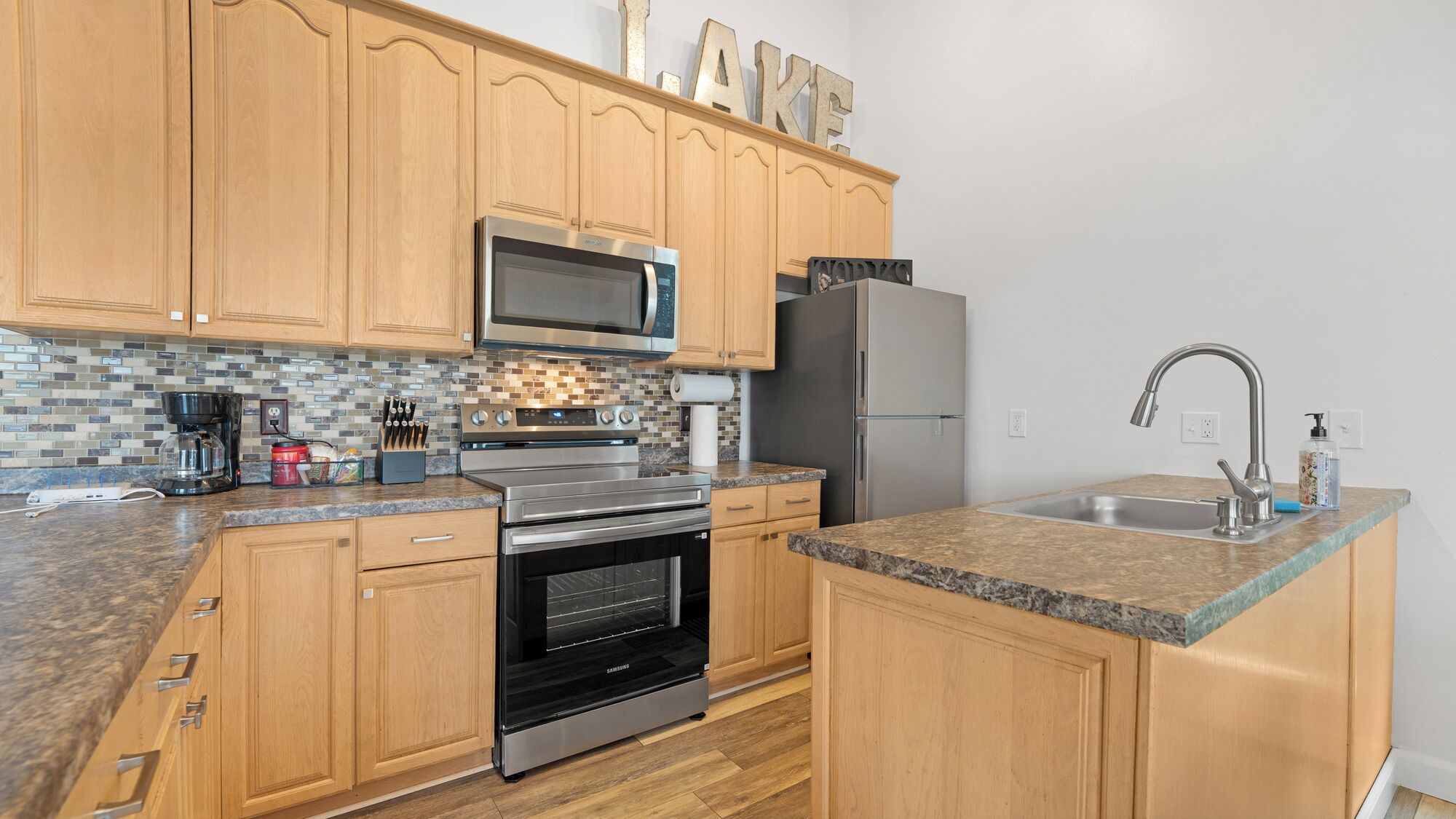 A kitchen with wooden cabinets, stainless steel appliances, a granite countertop, and a tiled backsplash.