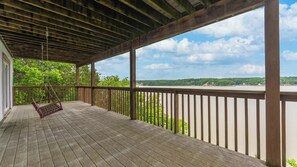 Eine Holzterrasse mit einer Schaukel, mit Blick auf einen Fluss und viel Grün.