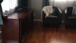 A living room with a wooden cabinet, a television, two leather chairs, and a clock on the wall. - Luxury & Dog Friendly (Nelson)