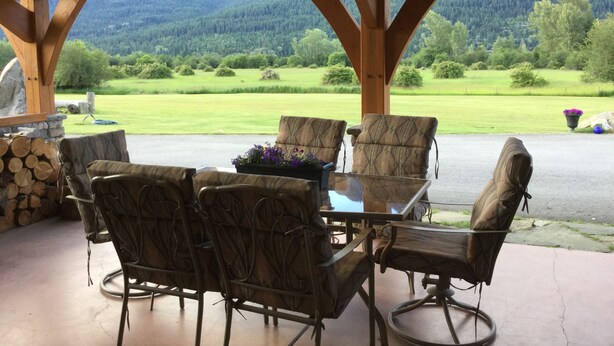 A covered patio with a table and chairs, a stone wall, and a view of a green landscape with trees and a mountain in the distance. - Luxury & Dog Friendly (Nelson)