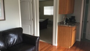 A living room with a black leather couch, wooden flooring, and a kitchen area with wooden cabinets and a countertop. - Luxury & Dog Friendly (Nelson)