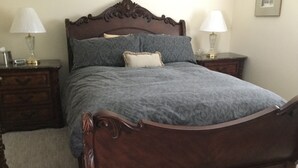 A bedroom with a wooden bed frame, two bedside tables with lamps, a nightstand, and a framed picture on the wall. - Luxury & Dog Friendly (Nelson)