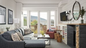 A modern living room with a grey sofa, a red armchair, a coffee table, and a fireplace with a wooden log display.