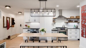 A modern kitchen with white cabinetry, a central island with seating, a built-in oven, and a hanging light fixture.