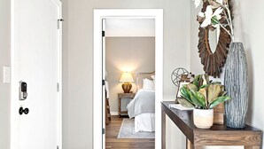 A hallway leading to a bedroom with a bed, bedside table, lamp, and decorative items. - Bright, Cozy Riverfront Condo walkable to Downtown Nashville! (Nashville)