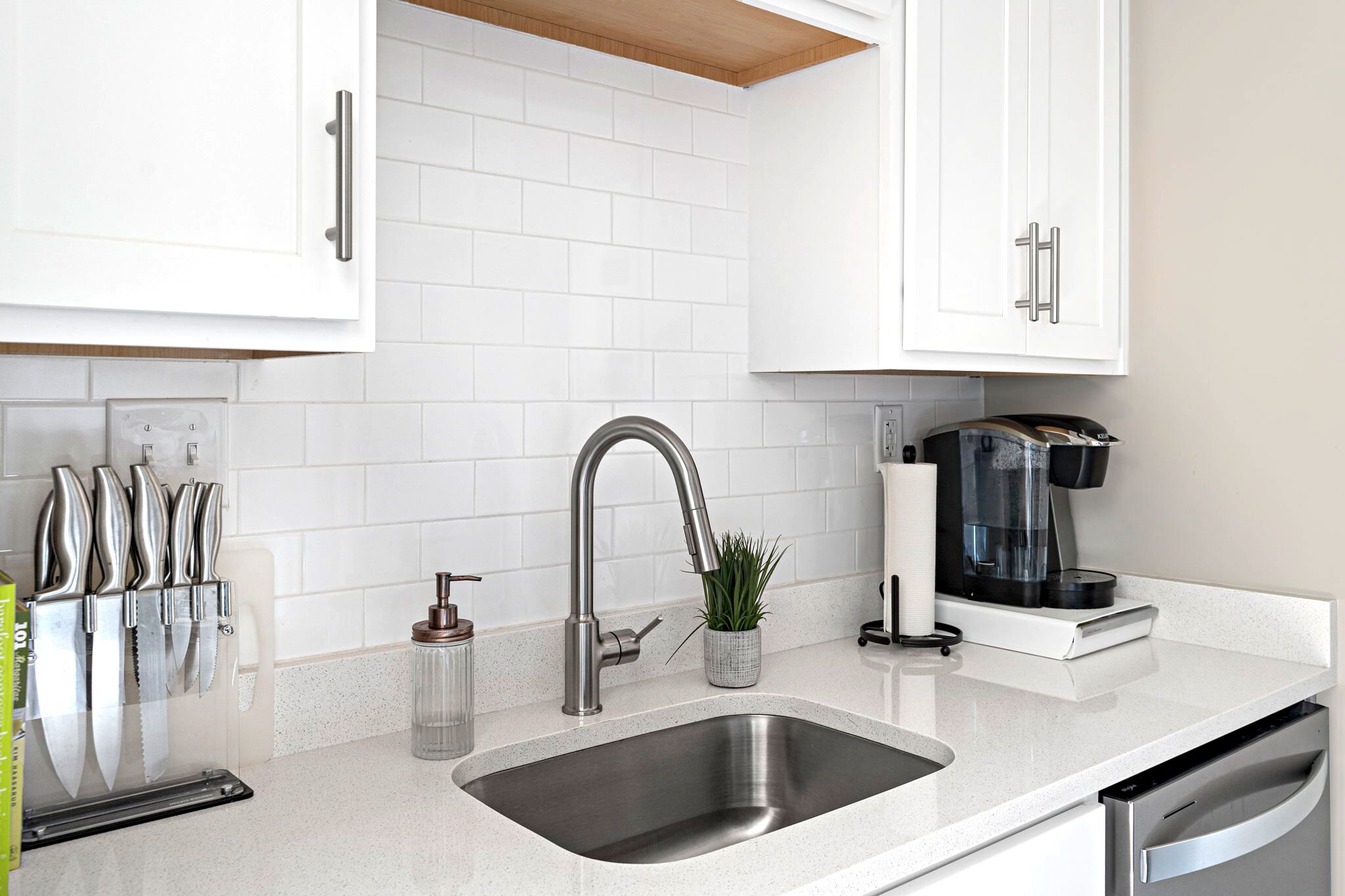 A modern kitchen with white cabinets, a stainless steel sink, and a coffee maker.