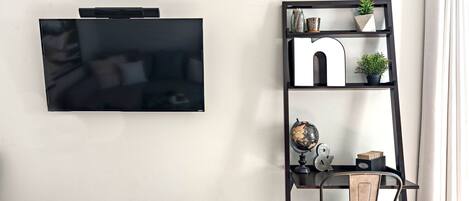 Ein modernes Wohnzimmer mit flachbildfernseher an der Wand, einem hölzernen Bücherregal mit Dekorationen und einem Vintage-Sessel.