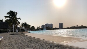 Una playa con cielo despejado, palmeras y edificios al fondo.