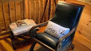 En mysig stuga med trägolv, en gungstol med en kudde, en lampa, en tavla och en karta på väggen.