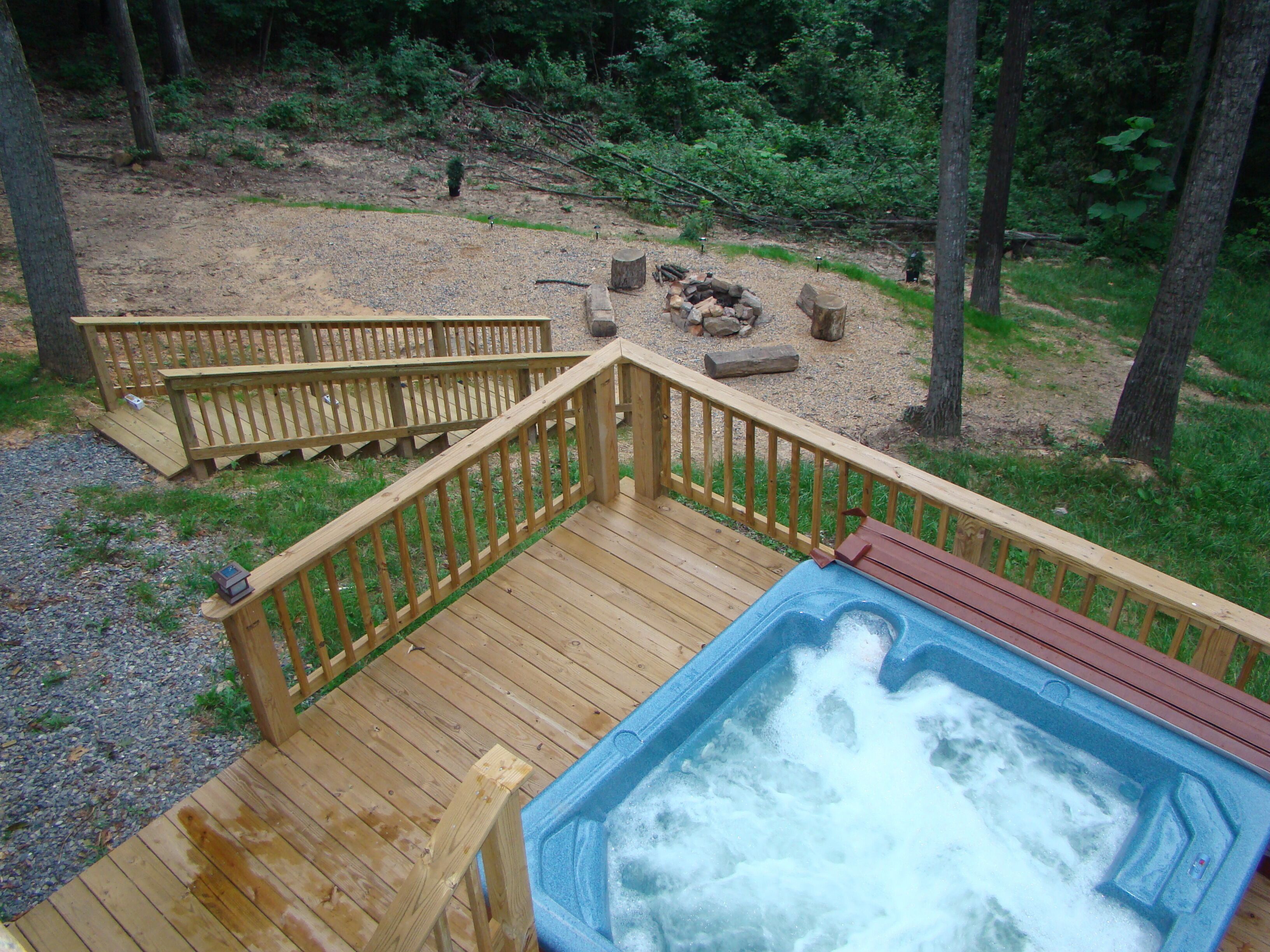 A wooden deck with a hot tub and a fire pit in the background.
