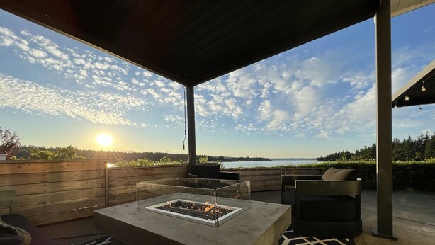 An outdoor patio with a fire pit, seating, and a view of the sunset over the water. - End of The Point - Main House (Bremerton)