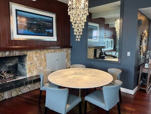 Un comedor con chimenea de piedra, una mesa redonda con seis sillas y un espejo grande que refleja la habitación.