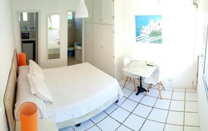 A bedroom with a bed, a small table with a chair, a window with a painting, and a bathroom visible through an open door. - Hotel Club De La Barra (Punta del Este)