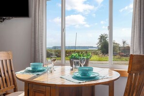 A dining table with teal tableware and glasses, a wooden chair, and a view of a green landscape through large windows.