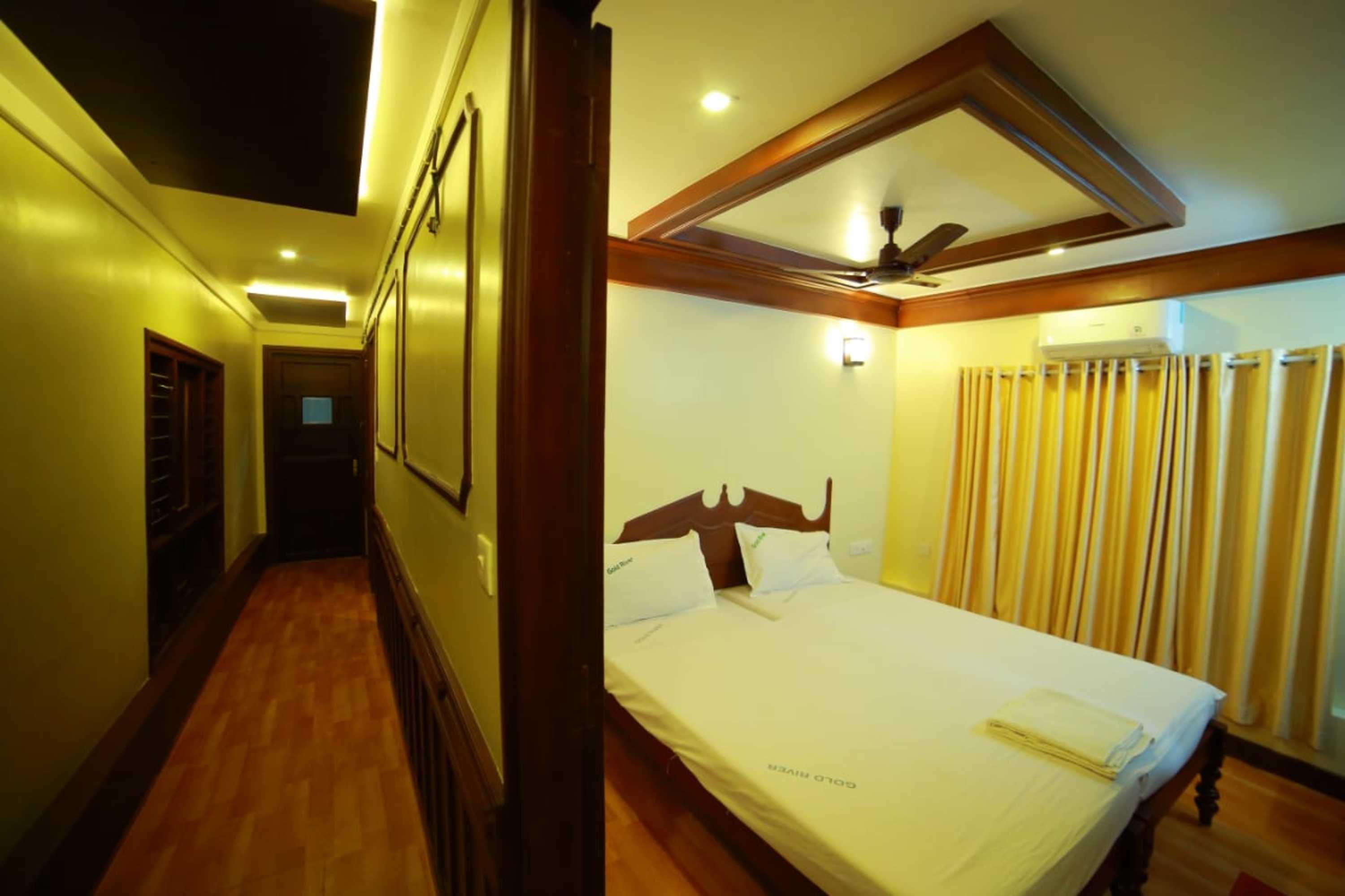 Habitación de hotel con cama, ventilador de techo, ventana con cortinas y piso de madera.