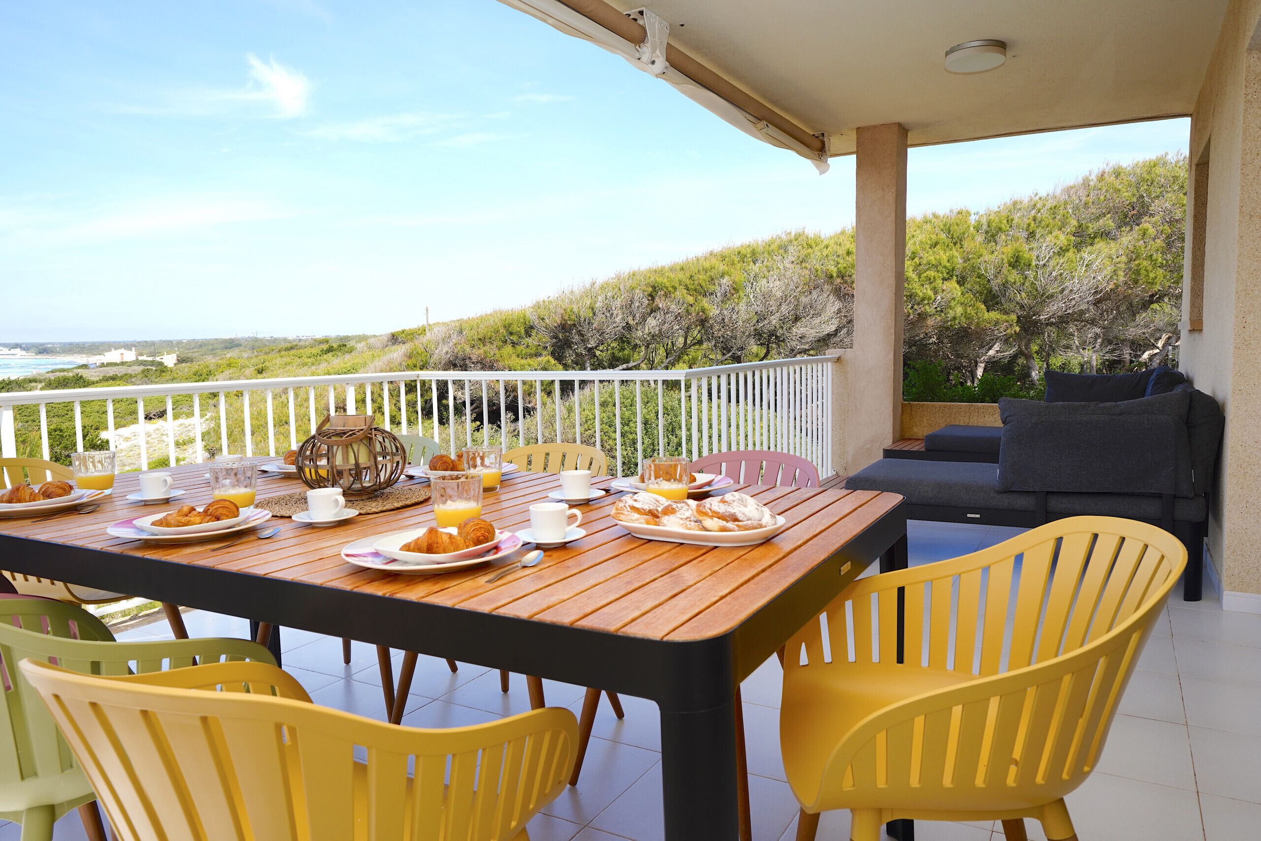 A breakfast table set with plates of food, cups, and a view of the sea.